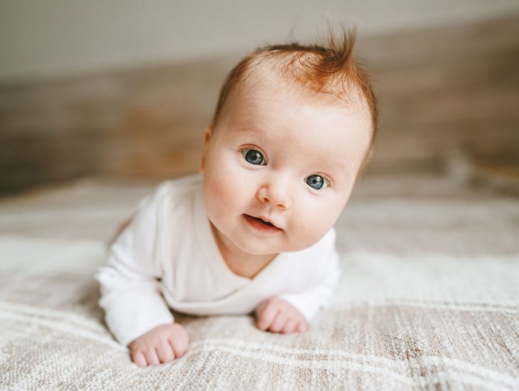 Cute baby ginger hair close up crawling on bed smiling adorable kid portrait family lifestyle 3 month old child