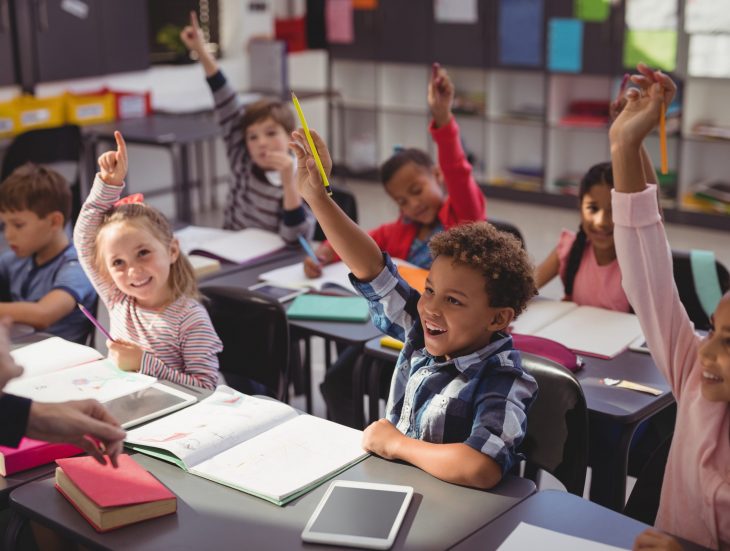 Schoolkids raising their hands in classroom